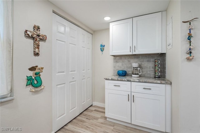 bar featuring light stone counters, backsplash, white cabinetry, and light wood-type flooring