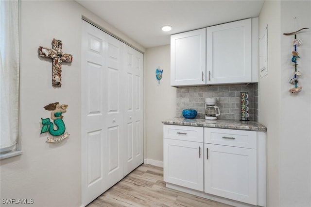 bar featuring light wood-style floors, baseboards, and decorative backsplash
