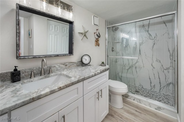 bathroom with vanity, a marble finish shower, wood finished floors, and toilet