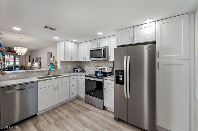 kitchen featuring white cabinets, stainless steel appliances, sink, backsplash, and a notable chandelier