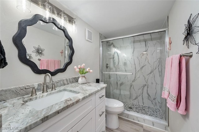 bathroom featuring a shower with shower door, vanity, and toilet