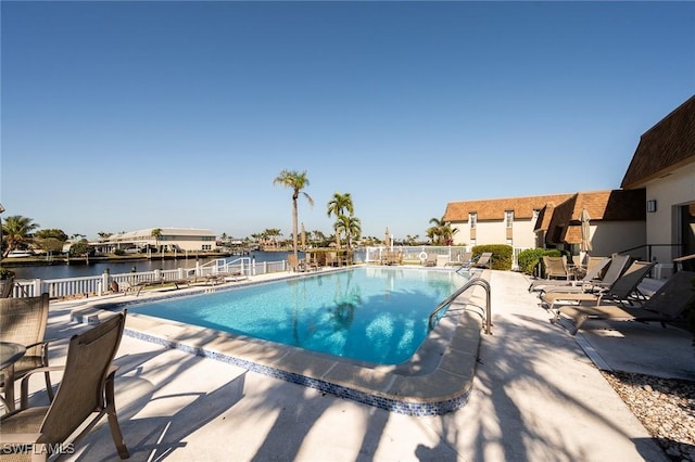 community pool with fence, a patio, and a water view