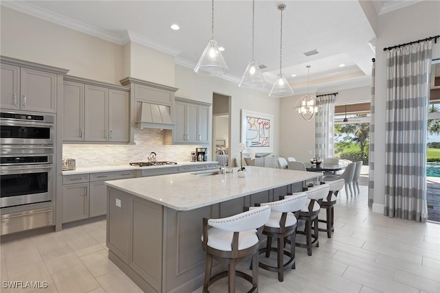 kitchen with light stone countertops, premium range hood, stainless steel appliances, sink, and gray cabinets