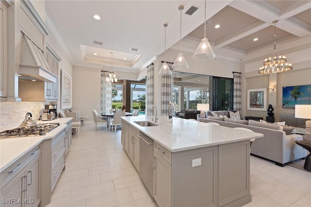 kitchen with a center island with sink, sink, hanging light fixtures, light stone counters, and stainless steel appliances