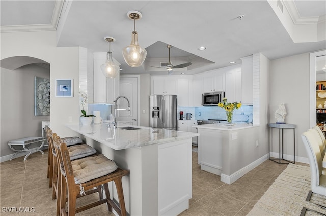 kitchen with crown molding, kitchen peninsula, a tray ceiling, white cabinetry, and stainless steel appliances