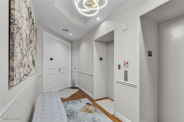 interior space featuring a tray ceiling, elevator, crown molding, and light hardwood / wood-style floors