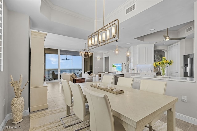 tiled dining area featuring floor to ceiling windows, sink, a raised ceiling, ceiling fan with notable chandelier, and ornamental molding