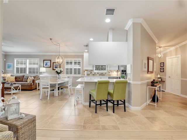 kitchen featuring crown molding, a breakfast bar area, light countertops, visible vents, and a chandelier