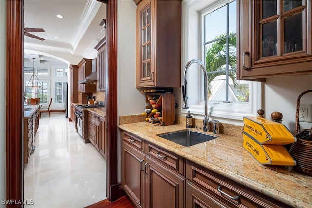 kitchen with ceiling fan, light stone countertops, ornamental molding, high end stainless steel range, and sink