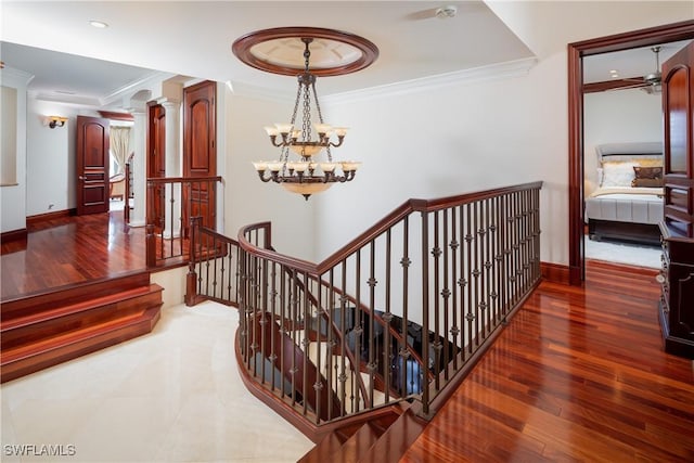 staircase with hardwood / wood-style flooring, crown molding, and a notable chandelier