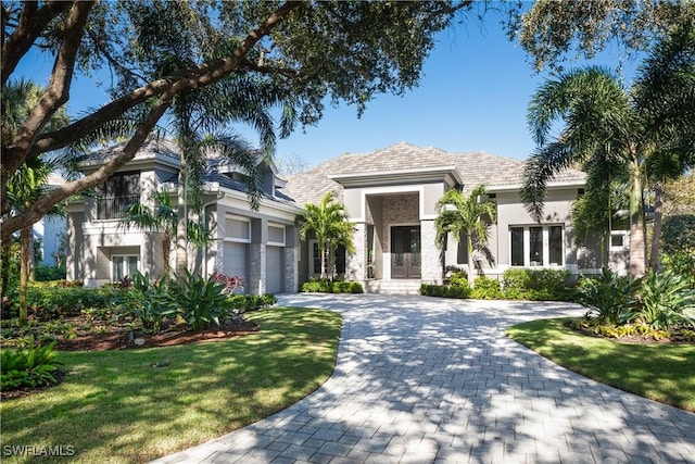 view of front of property with a front yard, stucco siding, french doors, a garage, and decorative driveway