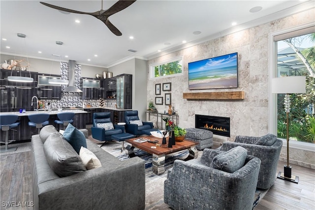 living area with a ceiling fan, recessed lighting, a fireplace, ornamental molding, and light wood-type flooring