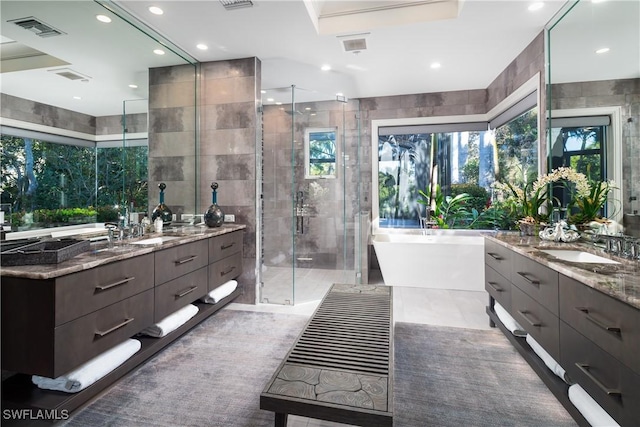 bathroom featuring visible vents, two vanities, a stall shower, tile walls, and a sink