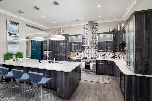 kitchen featuring crown molding, wall chimney range hood, light countertops, stainless steel range, and a sink