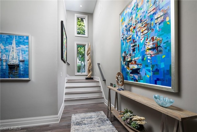 stairway with baseboards, wood finished floors, and a towering ceiling