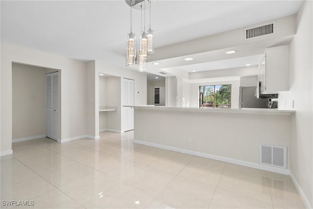 kitchen with kitchen peninsula, light tile patterned floors, decorative light fixtures, white cabinetry, and stainless steel refrigerator