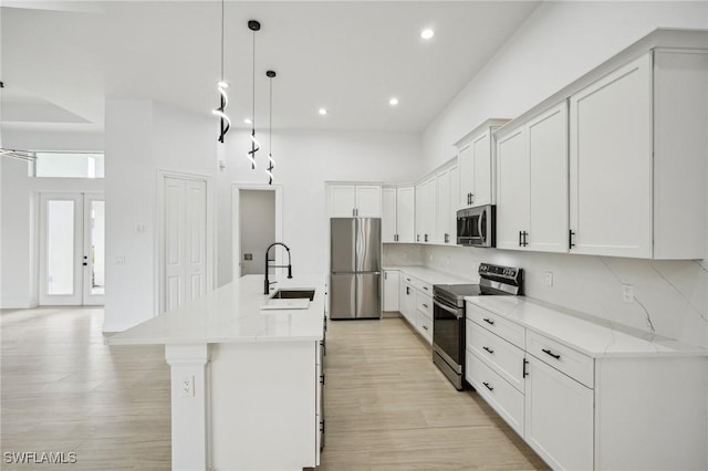 kitchen featuring a kitchen island with sink, hanging light fixtures, sink, light stone counters, and stainless steel appliances