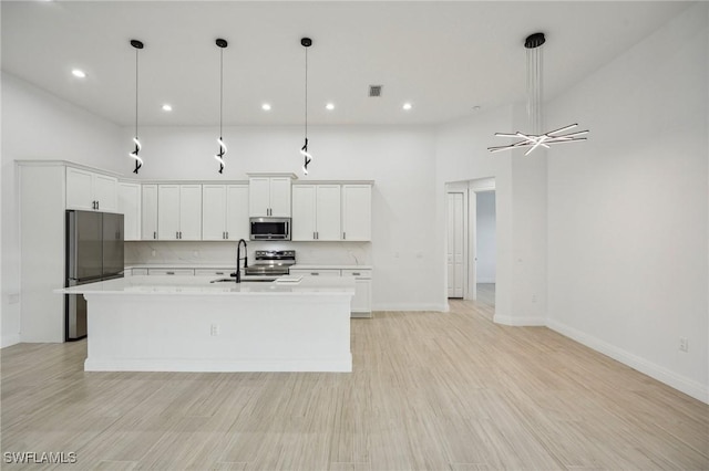 kitchen featuring pendant lighting, white cabinets, sink, an island with sink, and appliances with stainless steel finishes