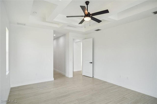 spare room with light wood-type flooring, a tray ceiling, and ceiling fan