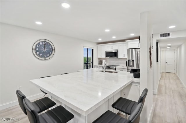 kitchen with white cabinetry, sink, stainless steel appliances, light hardwood / wood-style floors, and a breakfast bar