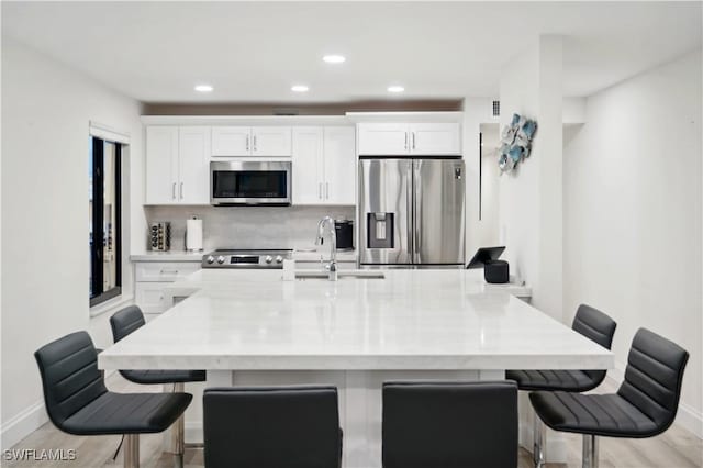 kitchen with a center island with sink, a kitchen bar, white cabinetry, and appliances with stainless steel finishes