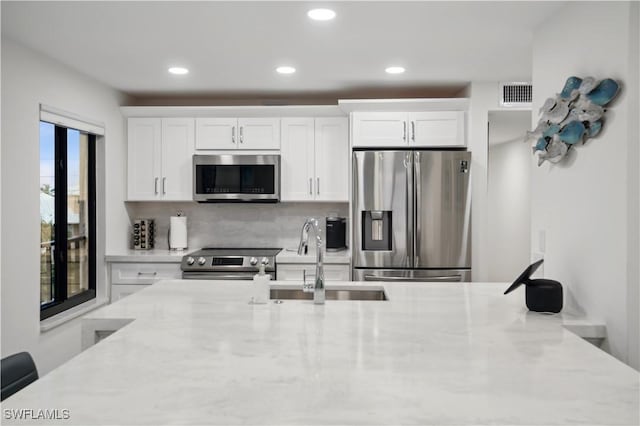 kitchen featuring white cabinets, sink, decorative backsplash, light stone countertops, and appliances with stainless steel finishes