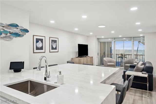 kitchen featuring light stone countertops, light wood-type flooring, floor to ceiling windows, and sink