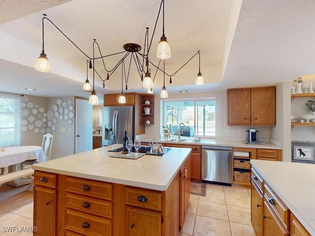 kitchen with appliances with stainless steel finishes, pendant lighting, sink, a center island, and a tray ceiling