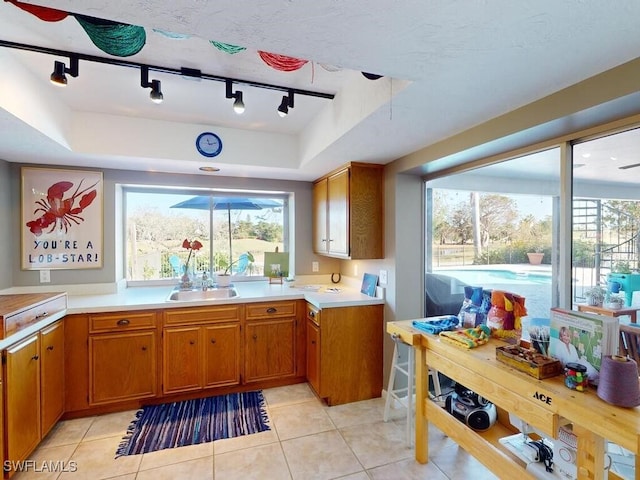 kitchen featuring rail lighting, sink, light tile patterned floors, and a tray ceiling