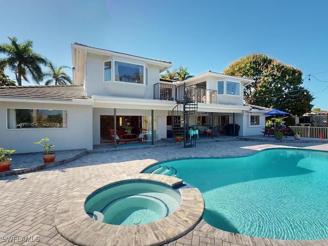 rear view of house featuring a balcony, a swimming pool with hot tub, and a patio