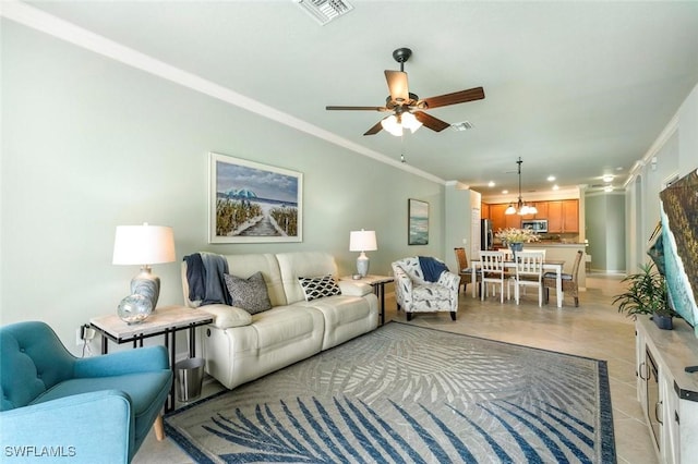 tiled living room with ceiling fan with notable chandelier and ornamental molding