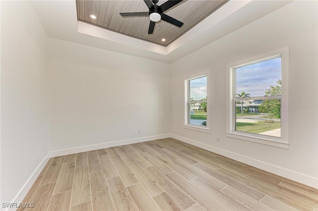 empty room with a tray ceiling, light hardwood / wood-style flooring, and ceiling fan