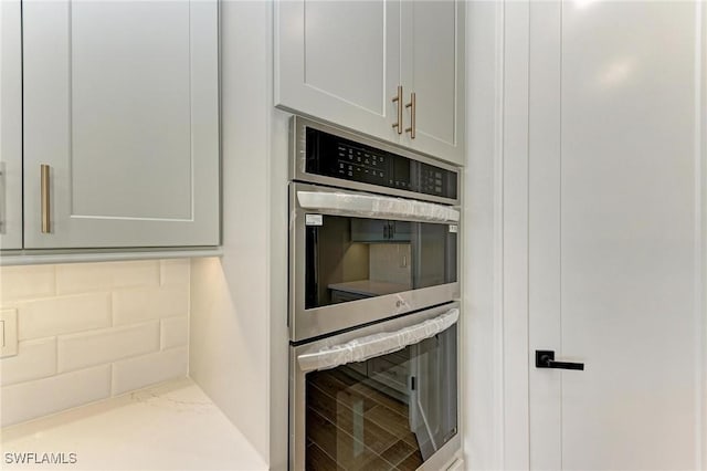 kitchen featuring double oven, backsplash, and light stone counters