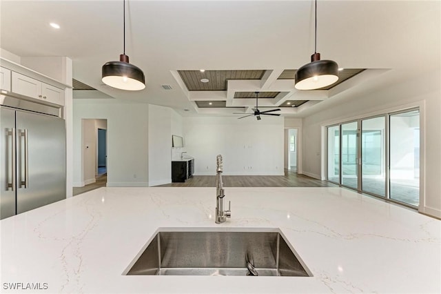 kitchen with ceiling fan, sink, built in fridge, light stone counters, and pendant lighting