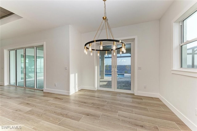 unfurnished dining area featuring a healthy amount of sunlight, french doors, and a chandelier