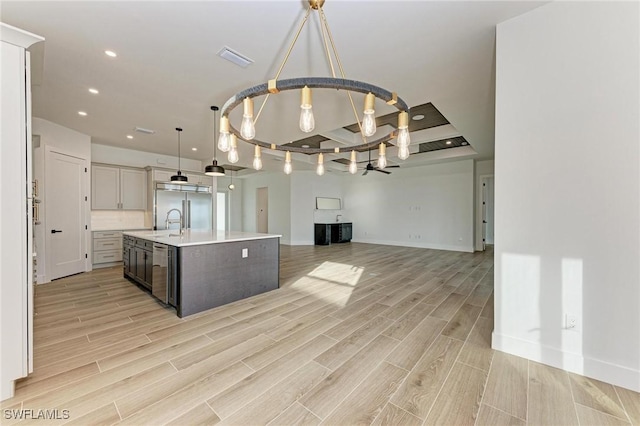 kitchen with appliances with stainless steel finishes, an island with sink, hanging light fixtures, and light wood-type flooring