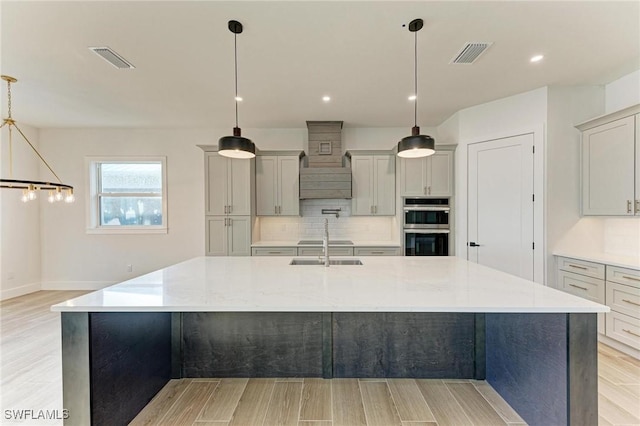 kitchen featuring decorative backsplash, a large island with sink, light wood-type flooring, and light stone counters