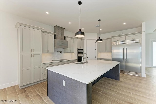 kitchen featuring stainless steel appliances, light stone counters, backsplash, an island with sink, and decorative light fixtures