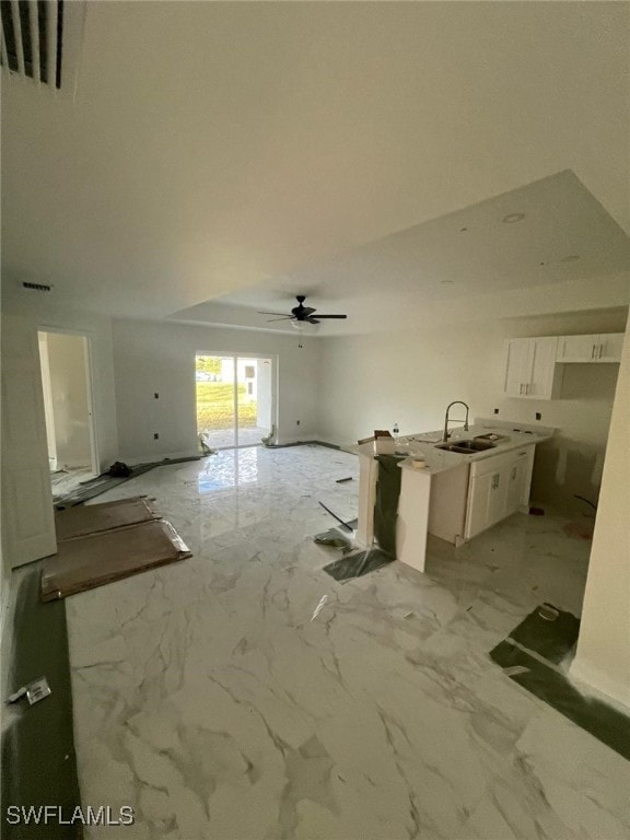 kitchen featuring ceiling fan, sink, white cabinetry, and an island with sink