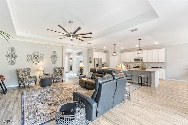 living room featuring light wood-type flooring, ceiling fan, crown molding, and a raised ceiling