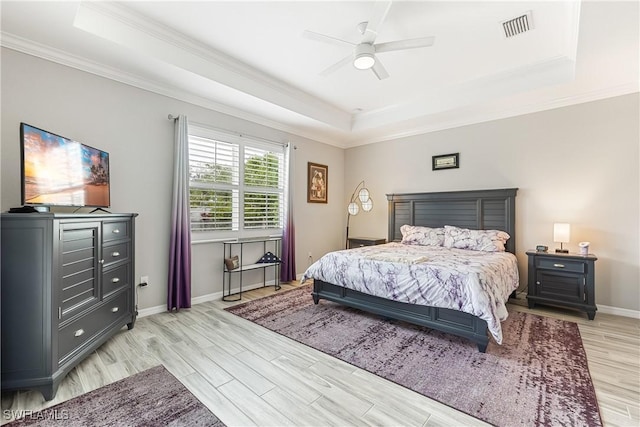 bedroom with ceiling fan, crown molding, a tray ceiling, and light hardwood / wood-style flooring