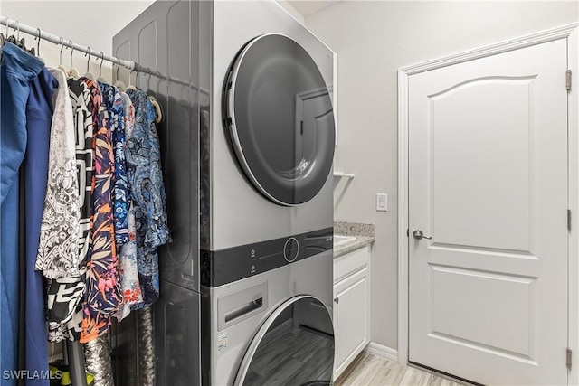 laundry area with cabinets, stacked washer and clothes dryer, and light hardwood / wood-style flooring