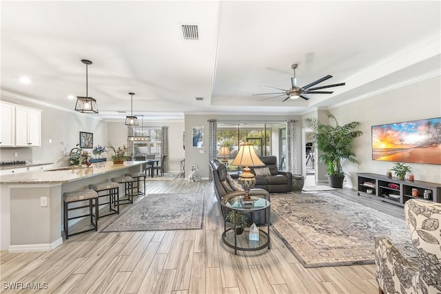 living room featuring ceiling fan, crown molding, a tray ceiling, and sink