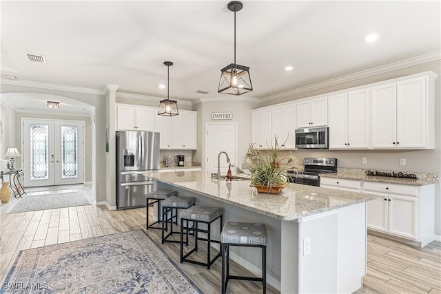 kitchen with white cabinets, appliances with stainless steel finishes, french doors, an island with sink, and sink