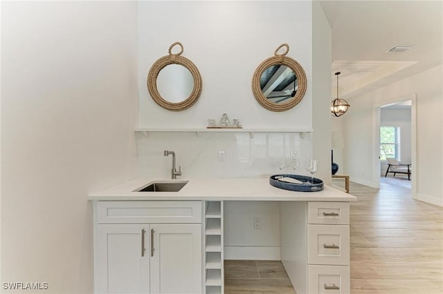 interior space featuring tasteful backsplash, sink, light hardwood / wood-style flooring, white cabinets, and hanging light fixtures