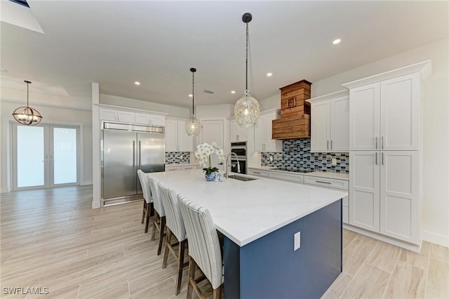 kitchen featuring a center island with sink, white cabinets, decorative light fixtures, and appliances with stainless steel finishes