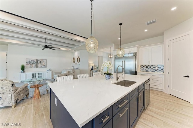 kitchen with a kitchen island with sink, white cabinets, sink, tasteful backsplash, and stainless steel appliances