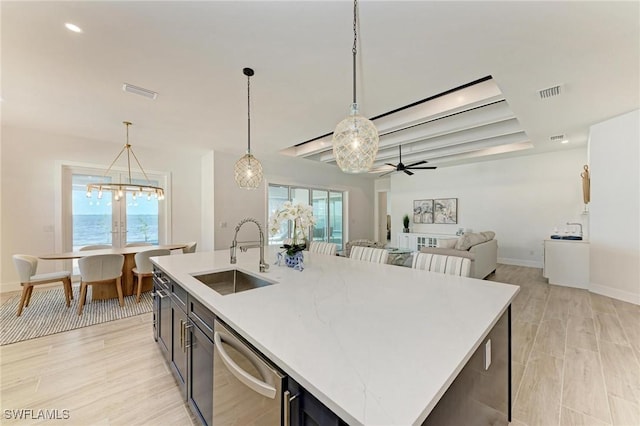 kitchen with pendant lighting, dishwasher, a center island with sink, ceiling fan with notable chandelier, and sink