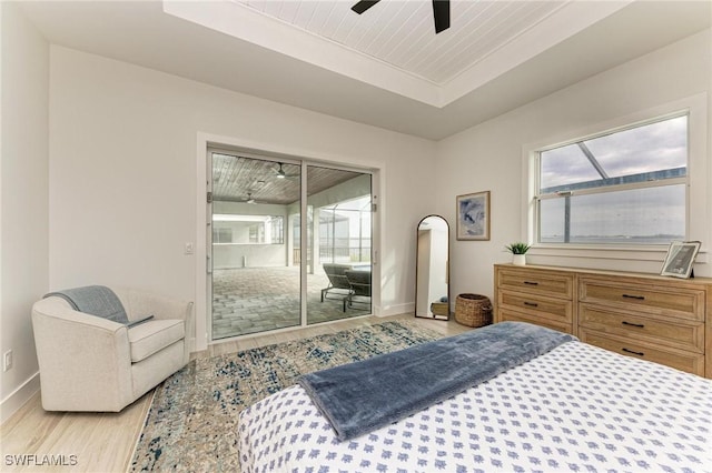 bedroom with ceiling fan, light hardwood / wood-style flooring, access to outside, and a tray ceiling