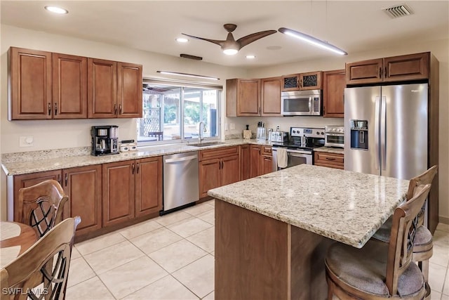 kitchen with light stone counters, stainless steel appliances, ceiling fan, light tile patterned flooring, and sink